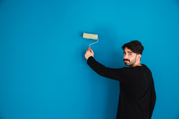 Man painting a bright blue wall with a roller brush, symbolizing activities in the coatings and plastics markets